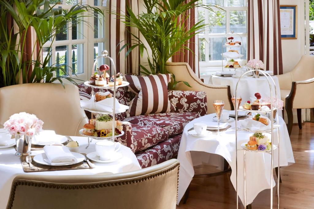 Mesas postas para o chá da tarde com bandejas de bolos e petiscos em uma sala iluminada e elegante com grandes janelas, na propriedade do The Montague On The Gardens.