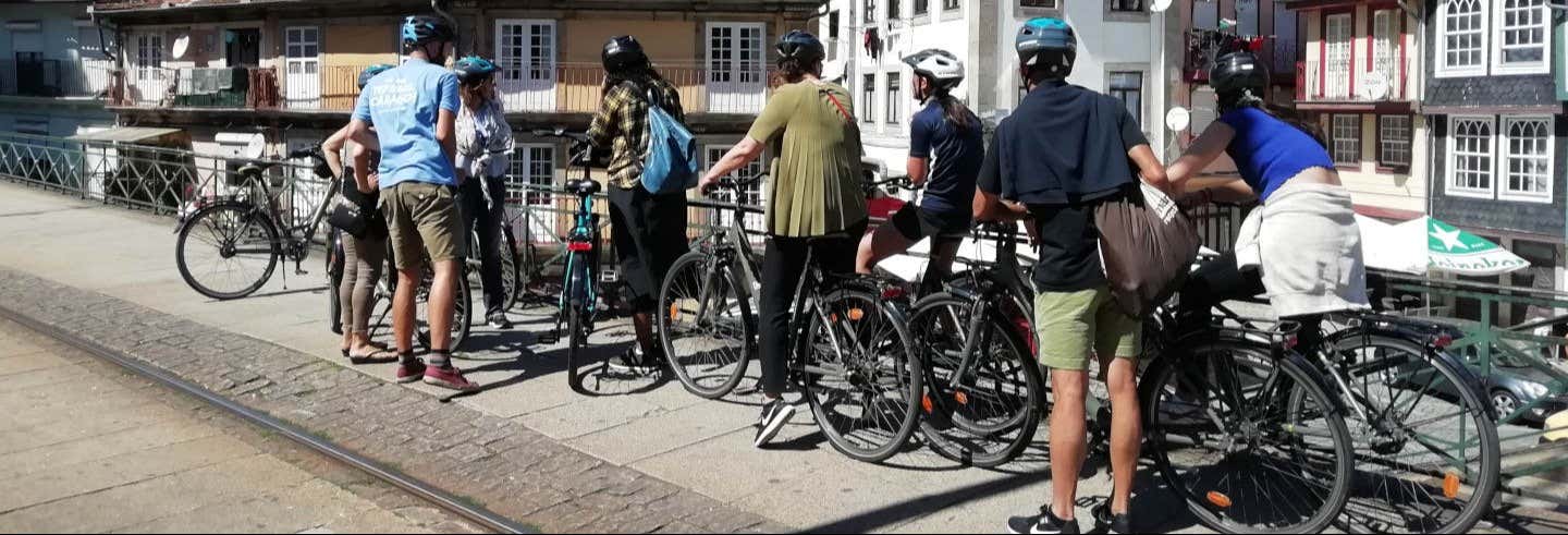 Um grupo de pessoas usando capacetes está parado com suas bicicletas em uma ponte em uma área urbana com edifícios ao fundo. A foto é capa do post Tour de bicicleta elétrica pelo Porto.