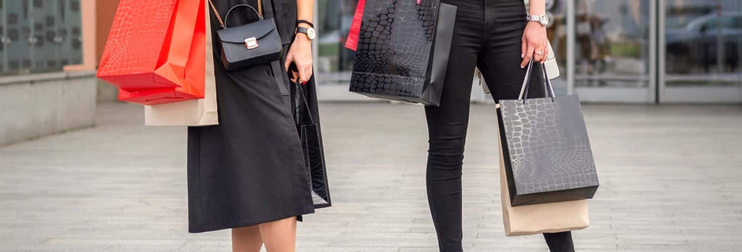 Duas pessoas segurando sacolas de compras estão do lado de fora de um prédio, apenas a parte inferior do corpo e as sacolas estão visíveis. A foto é capa do post do Tour de compras pelos outlets.