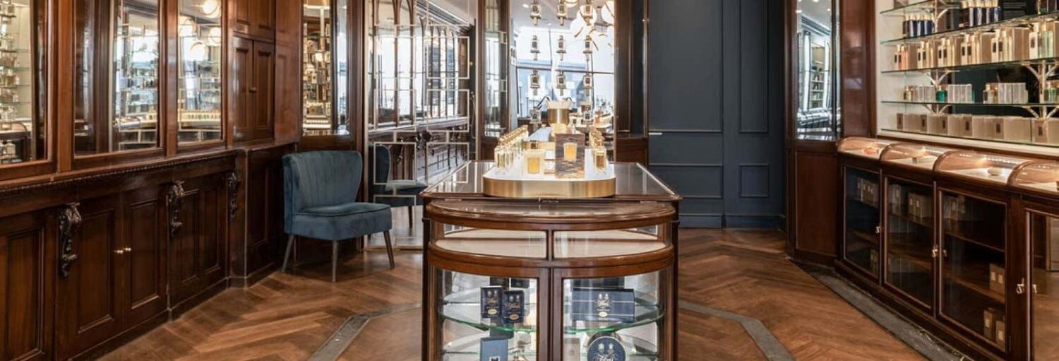 Uma loja de perfumes de luxo com armários de madeira, vitrines de vidro e prateleiras cheias de vários frascos de perfume.