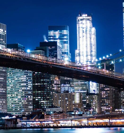 A Ponte do Brooklyn à noite com o horizonte iluminado da cidade de Nova York ao fundo.
