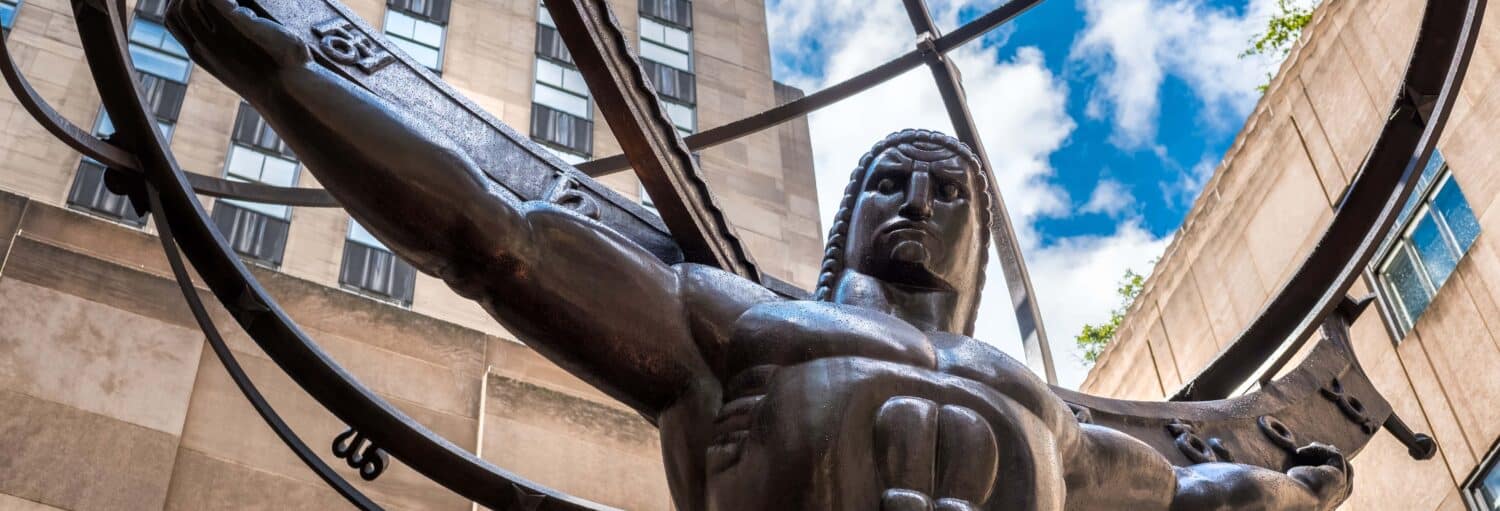 Visão ampliada da estátua de Atlas segurando um grande globo, com edifícios e céu azul ao fundo. A foto é capa do post de Tour pelo Rockefeller Center.