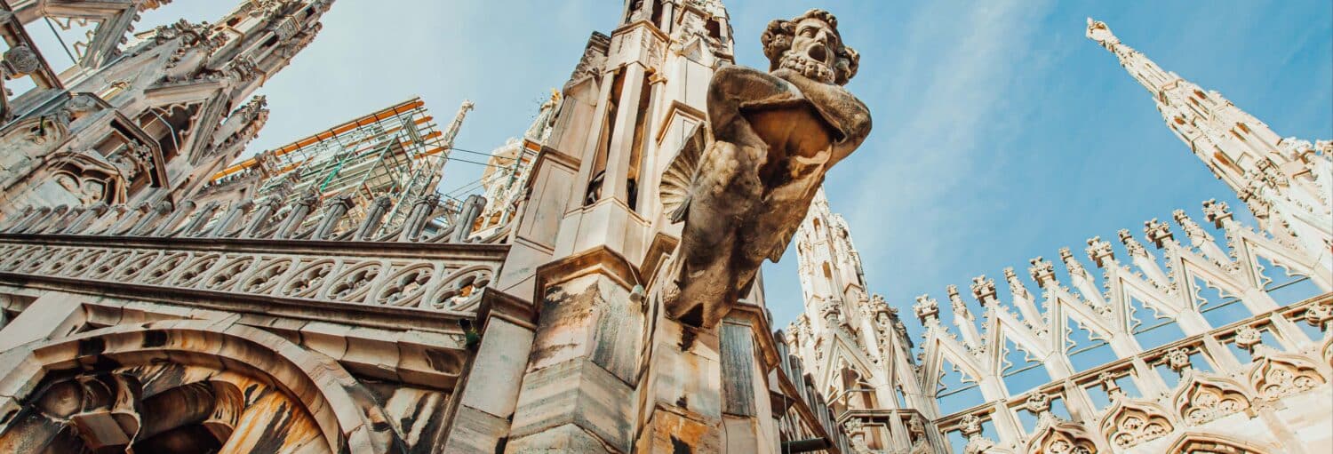 Imagem de um castelo imponente, onde uma de suas torres possui uma estátua. Tour pelos terraços do Duomo