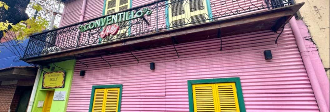 Um edifício rosa com persianas amarelas, uma porta verde e uma varanda com uma placa que diz "Conventillo 1906". Imagem para ilustrar post sobre almoço com espetáculo de tango + degustação de vinhos.