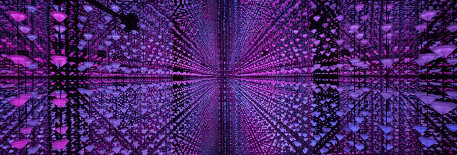 Um padrão geométrico de luzes roxas e rosa forma um efeito visual simétrico, semelhante a um túnel, com superfícies reflexivas. A imagem ilustra o post sobre visita guiada ao Museu Moco.
