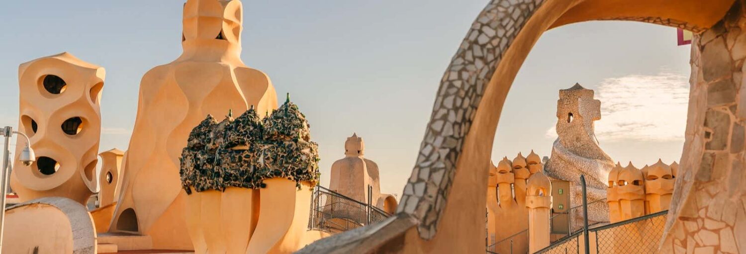 Telhado da Casa Milà em Barcelona, com chaminés esculturais e detalhes em mosaico sob um céu claro. A imagem ilustra o post sobre visita guiada por La Pedrera.
