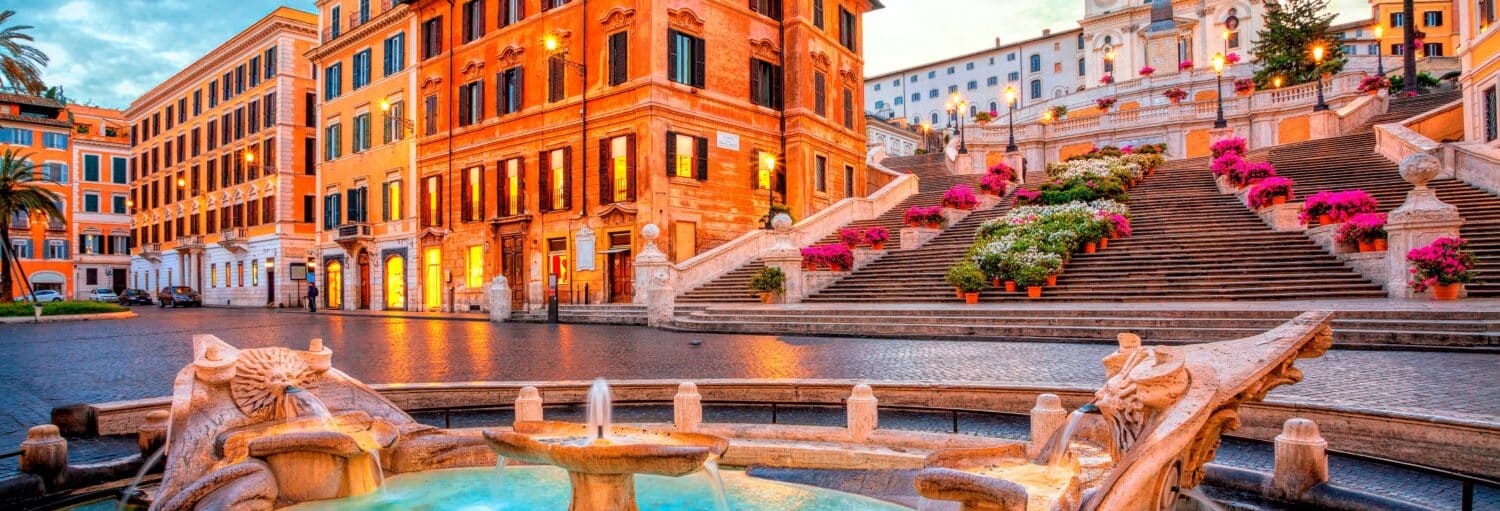 Uma fonte de pedra em frente à Escadaria Espanhola, ladeada por flores e cercada por edifícios coloridos ao pôr do sol na Visita guiada por Roma