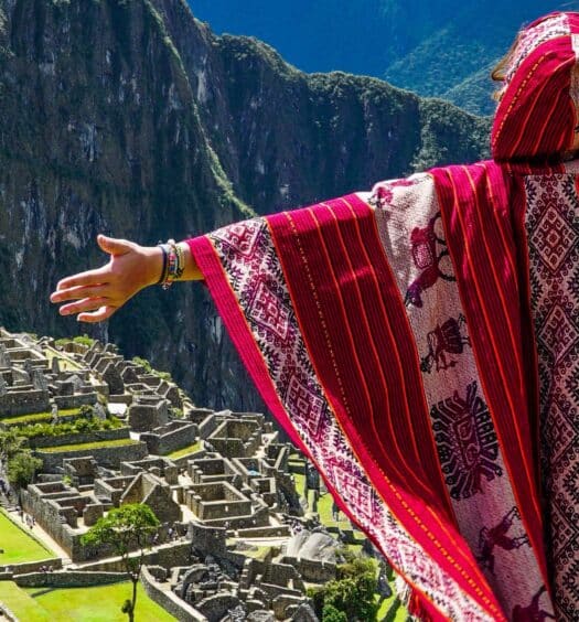 Uma pessoa vestindo roupas tradicionais vermelhas, com os braços estendidos, observa as ruínas de Machu Picchu, no Peru na Excursão de 2 dias a Machu Picchu com ingressos