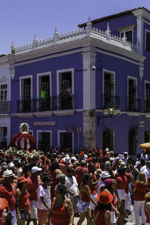 Uma multidão de pessoas vestidas de vermelho se reúne em frente a um edifício azul de estilo colonial em um dia ensolarado.