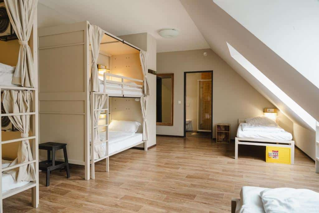 Um quarto espaçoso com beliches, uma cama de solteiro, piso de madeira e uma porta aberta que leva a outro quarto, no Wombat's City Hostel Vienna, para representar onde ficar em Viena.