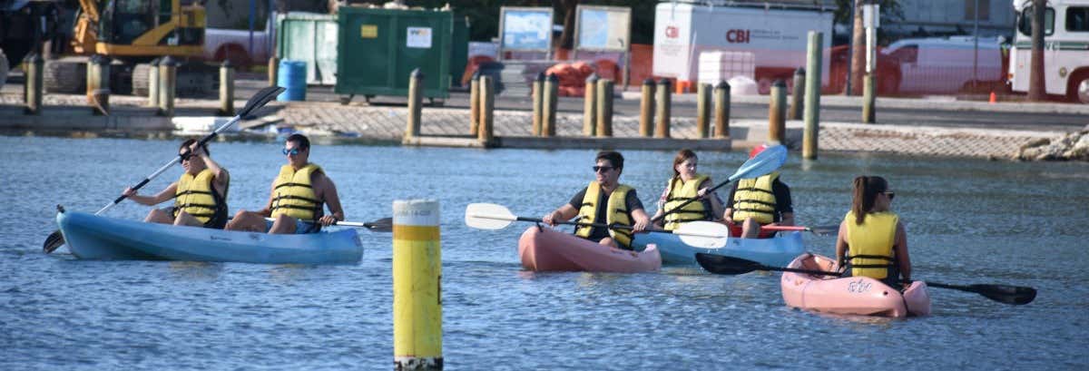 Seis pessoas com coletes amarelos andam de caiaque perto de uma doca com equipamentos de construção - Aluguel de paddle surf ou caiaque em Miami.