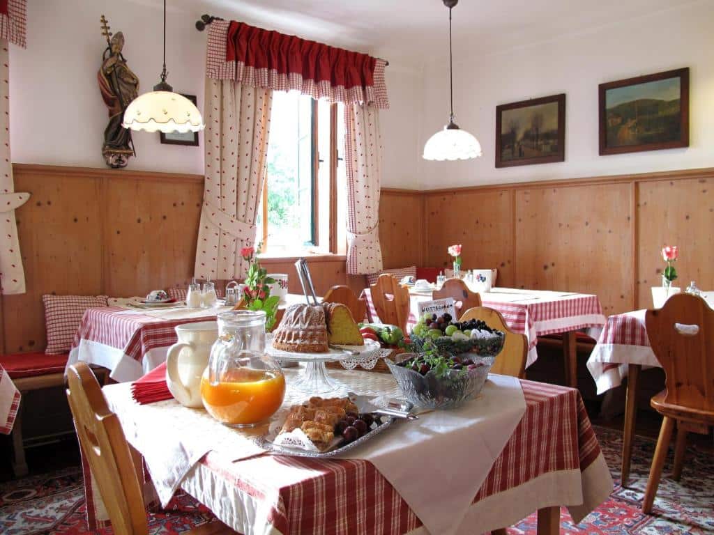 Uma sala de jantar aconchegante com paredes de madeira, toalhas de mesa xadrez vermelhas e mesas com alimentos e bebidas para o café da manhã, no Hotel Schneider-Gössl.