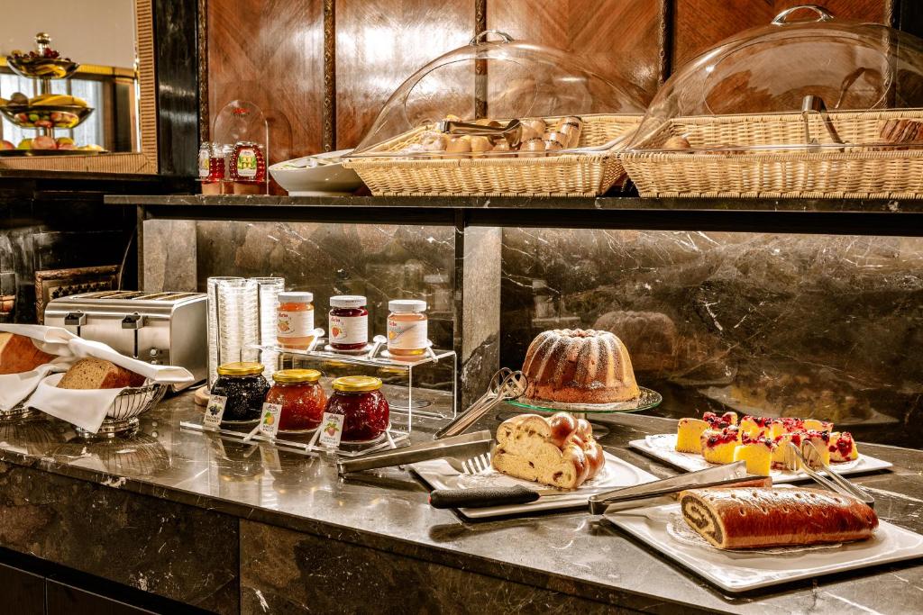 Um bufê de café da manhã com potes de geleia, pães, bolos, tortas, frutas cortadas e cestas cobertas em um balcão de mármore, no Hotel Erzherzog Rainer.