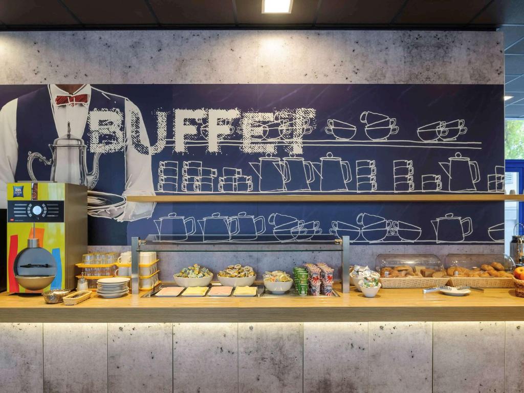 Buffet de café da manhã com doces, cereais, condimentos e uma máquina de bebidas quentes em um balcão de madeira com decoração temática de buffet, no Ibis budget Wien Sankt Marx.