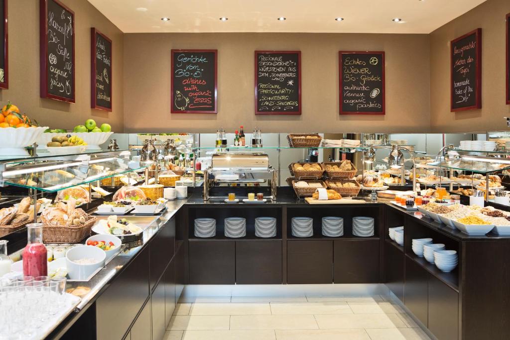 Buffet com vários alimentos para o café da manhã, pães, frutas e cardápios em quadro-negro na parede em uma área de jantar bem iluminada, no The Harmonie Vienna.