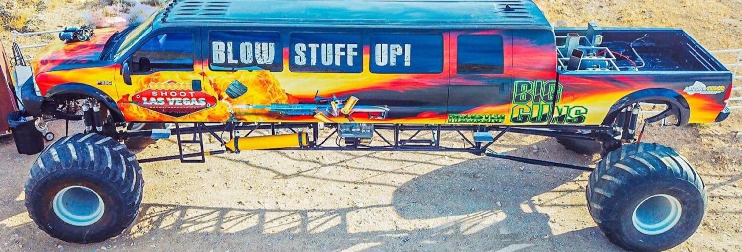 Um monster truck grande e personalizado com gráficos coloridos e pneus grandes estacionado em uma superfície de terra. Imagem para ilustrar post sobre condução de um monster truck no deserto de Las Vegas.