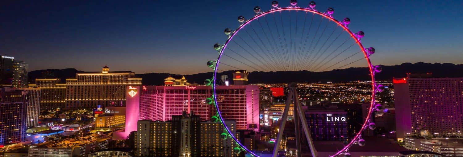 Vista noturna da Las Vegas Strip com a roda-gigante High Roller iluminada e os prédios de cassino bem iluminados. Imagem para ilustrar post sobre o ingresso da High Roller.