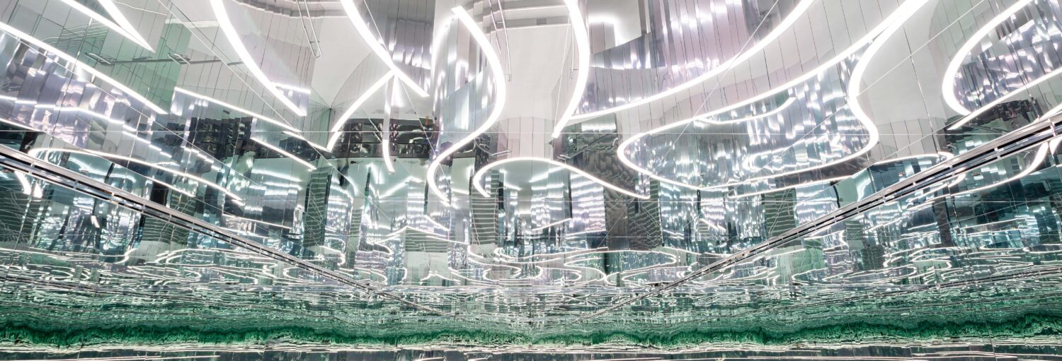 Luzes brancas curvas e superfícies metálicas reflexivas criam um efeito abstrato e espelhado em um espaço interno moderno. A imagem ilustra o post sobre Ingresso do Superblue Miami.