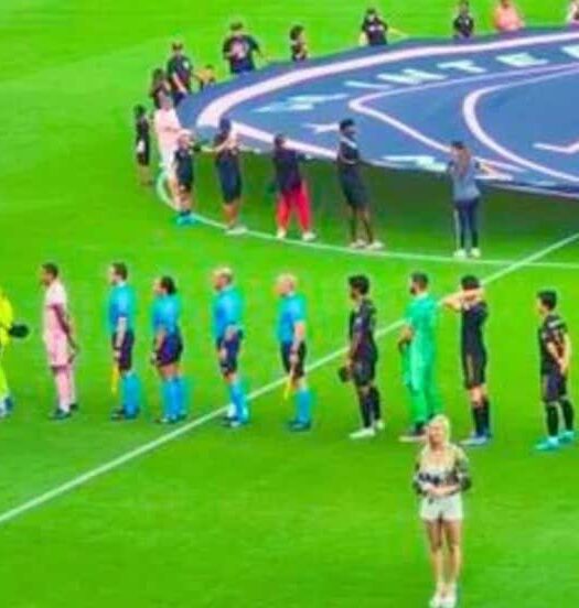 Dois times de futebol se alinham em um campo, um de frente para o outro, com oficiais entre eles e um grande logotipo do Inter Miami CF ao fundo. A imagem ilustra o post sobre Ingressos do jogo do Inter Miami CF.