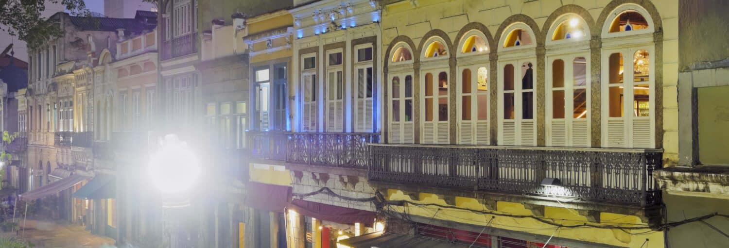 Uma fileira de edifícios históricos com janelas em arco brilha à noite, perto do espetáculo no Rio Scenarium.