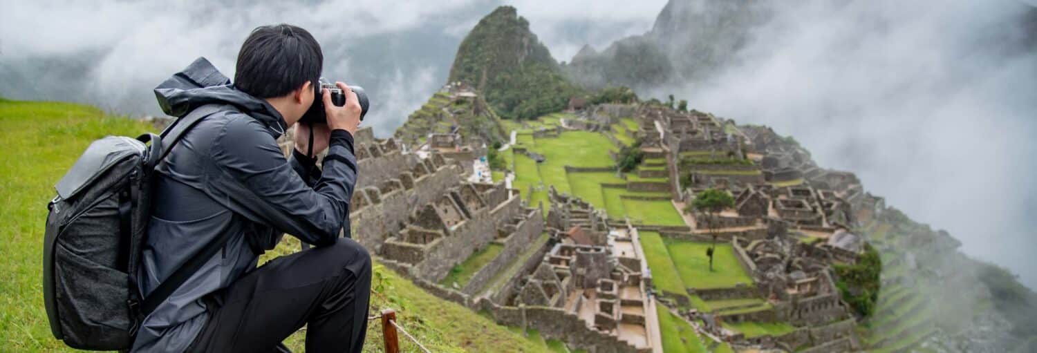 Uma pessoa com uma mochila tira uma foto das antigas ruínas incas de Machu Picchu em um dia de neblina na Excursão de 2 dias a Machu Picchu sem ingressos