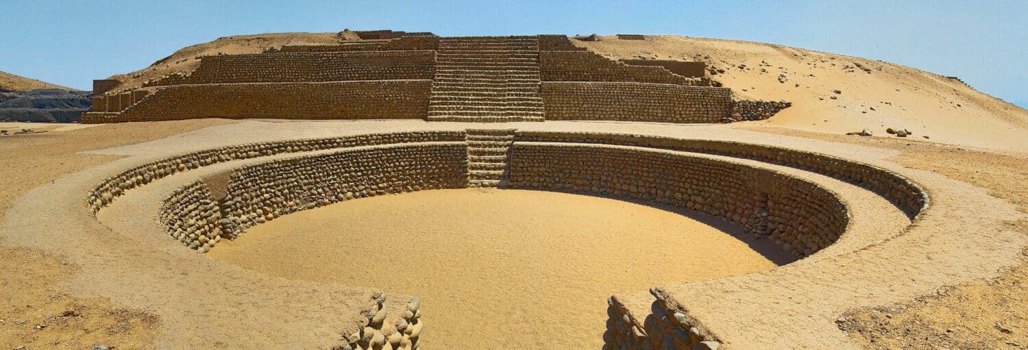 Antigo anfiteatro de pedra com degraus circulares e escada central em uma paisagem desértica sob um céu claro da Excursão a Bandurria e aos pântanos do Paraíso