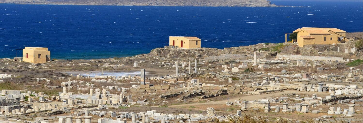 Um edifício em uma colina perto da água, com vista para o veleiro às ilhas de Delos e Rhenia.