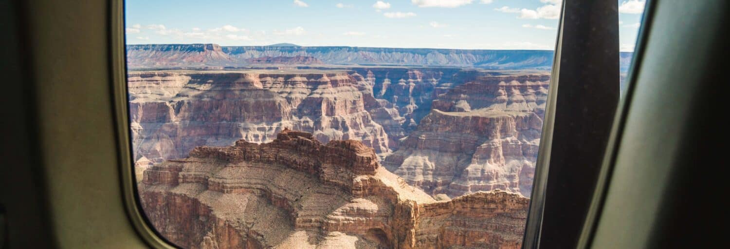 Vista das formações rochosas em camadas do Grand Canyon vista pela janela de um avião ou helicóptero sob um céu parcialmente nublado. Imagem para ilustrar post sobre passeio de monomotor pelo Grand Canyon.