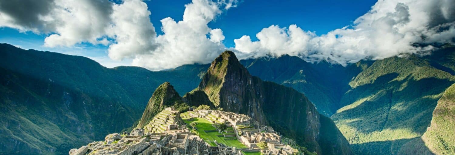 As ruínas de Machu Picchu ficam em um cume de montanha sob um céu azul com nuvens e montanhas verdes ao fundo na Excursão de 2 dias a Machu Picchu pela rota Abra Málaga