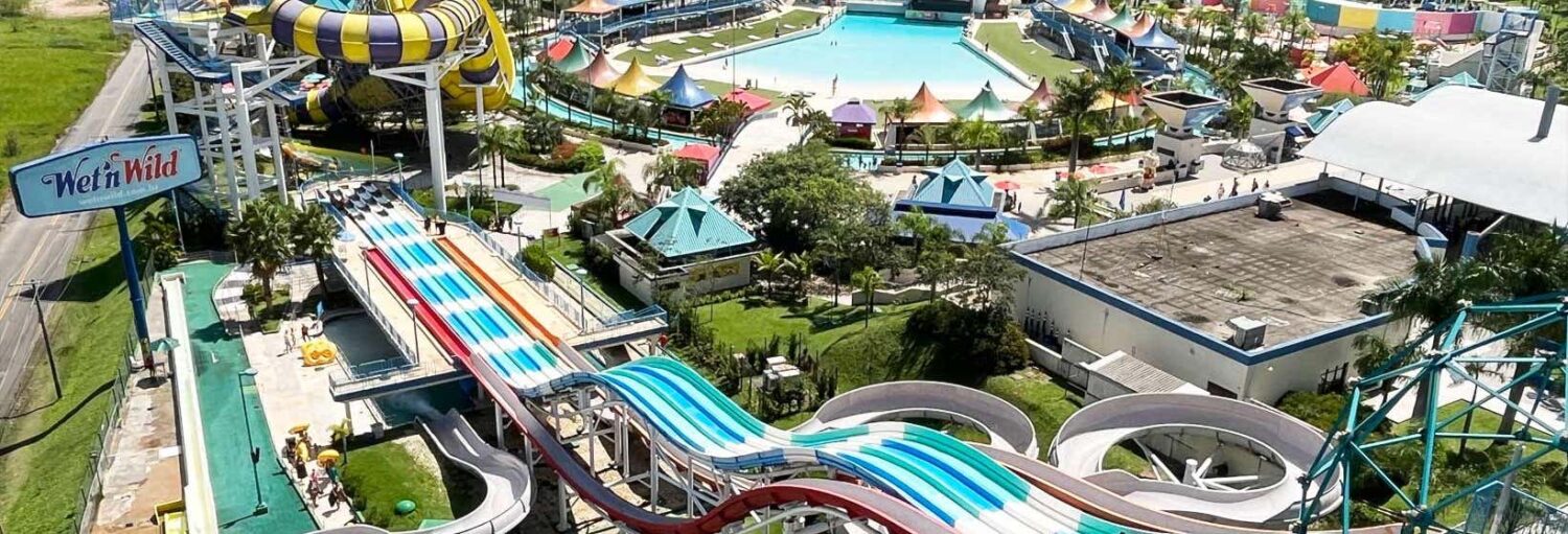 Vista aérea da Excursão ao Parque Aquático Wet'n Wild com escorregadores coloridos, piscina de ondas e espaços verdes exuberantes.