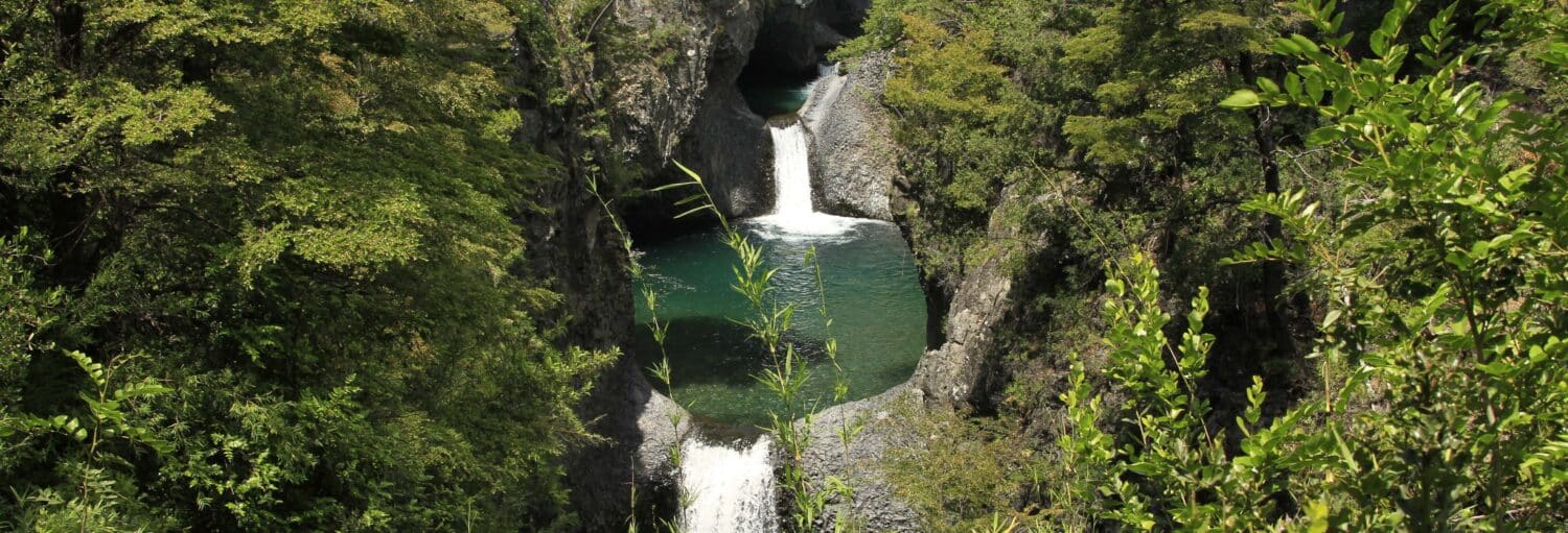 Uma cachoeira estreita cai em cascata em uma série de piscinas verdes cercadas por penhascos rochosos e vegetação densa. A foto é capa do post da Excursão ao Parque Nacional Siete Tazas.