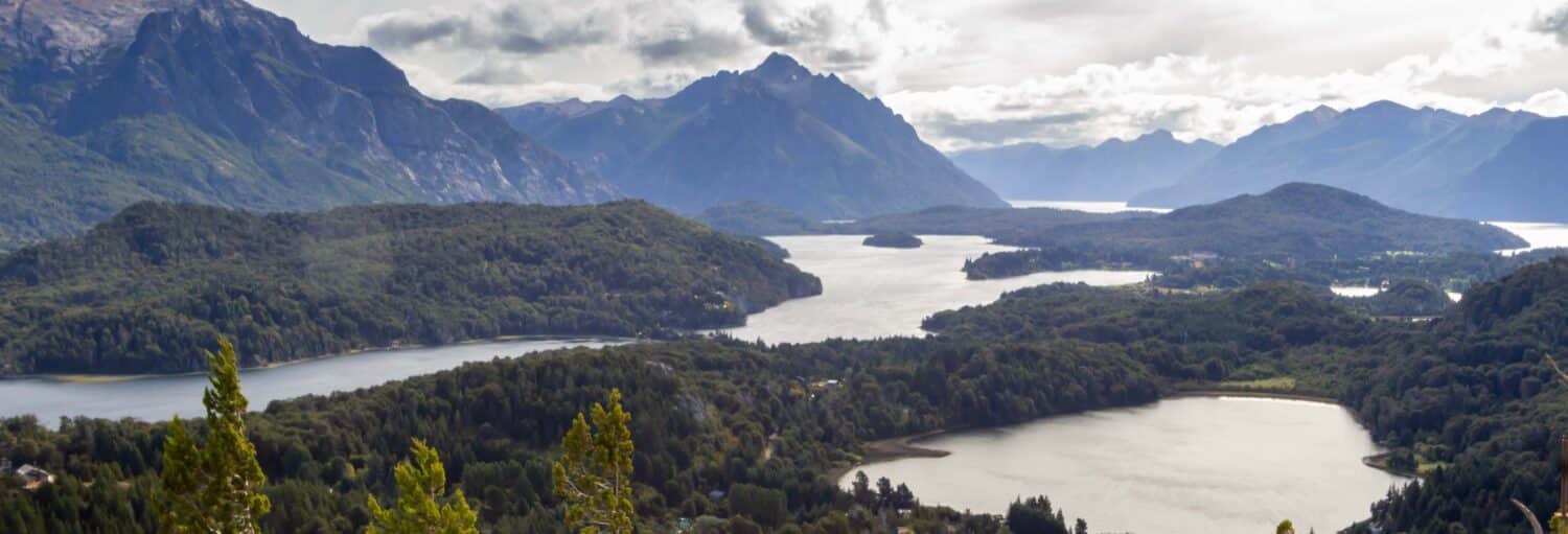 Um grande lago cercado por densas florestas e montanhas sob um céu parcialmente nublado da Excursão privada saindo de Bariloche