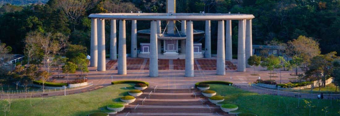 Grande monumento com colunas altas e jardins, apresentado na Excursão ao Solo Sagrado de Guarapiranga, cercado por árvores.