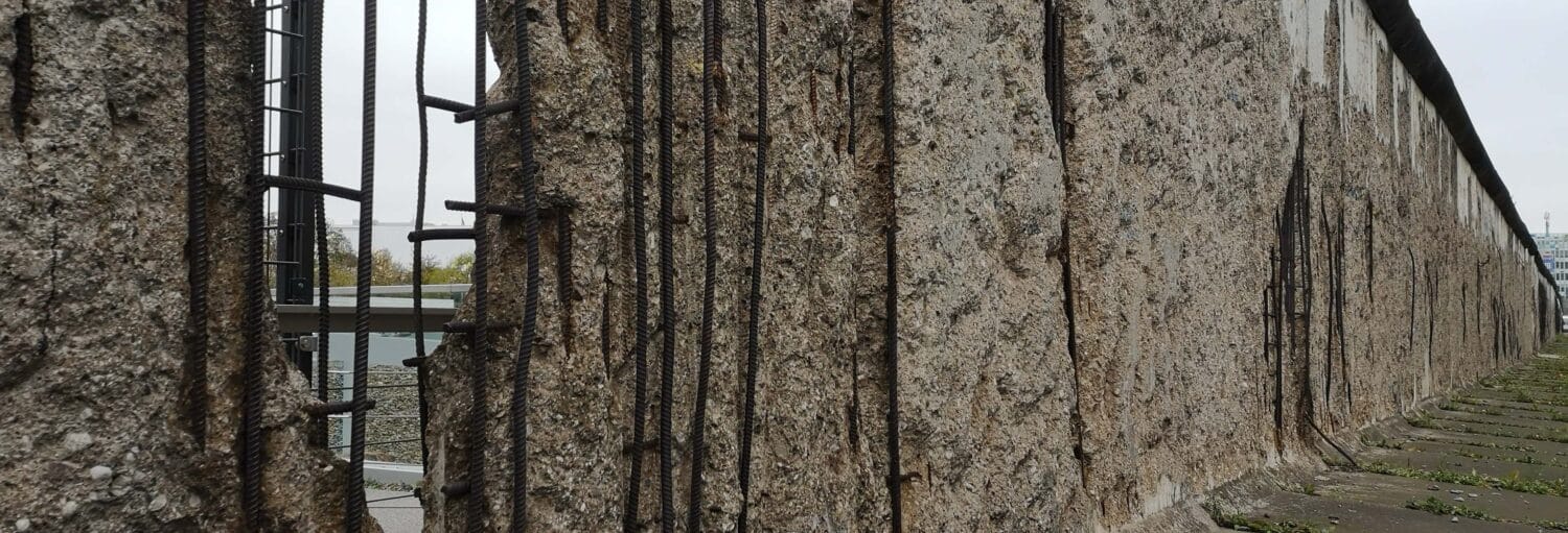 Um close-up de uma parede de concreto com vergalhões expostos, vista ao ar livre em um dia nublado. Imagem para ilustrar post sobre free tour do Muro de Berlim e da Guerra Fria.