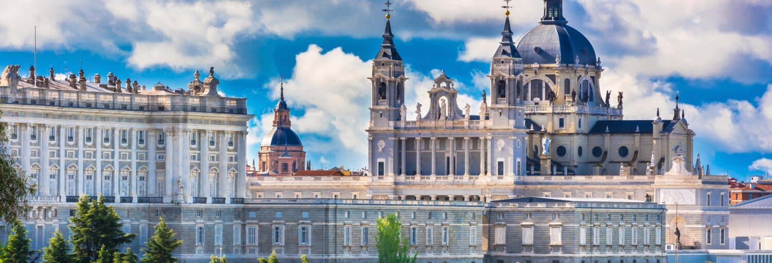 O Palácio Real e a Catedral de Almudena em Madri, Espanha, sob um céu azul parcialmente nublado. A imagem ilustra o post sobre Visita guiada Palácio Real e Catedral da Almudena.