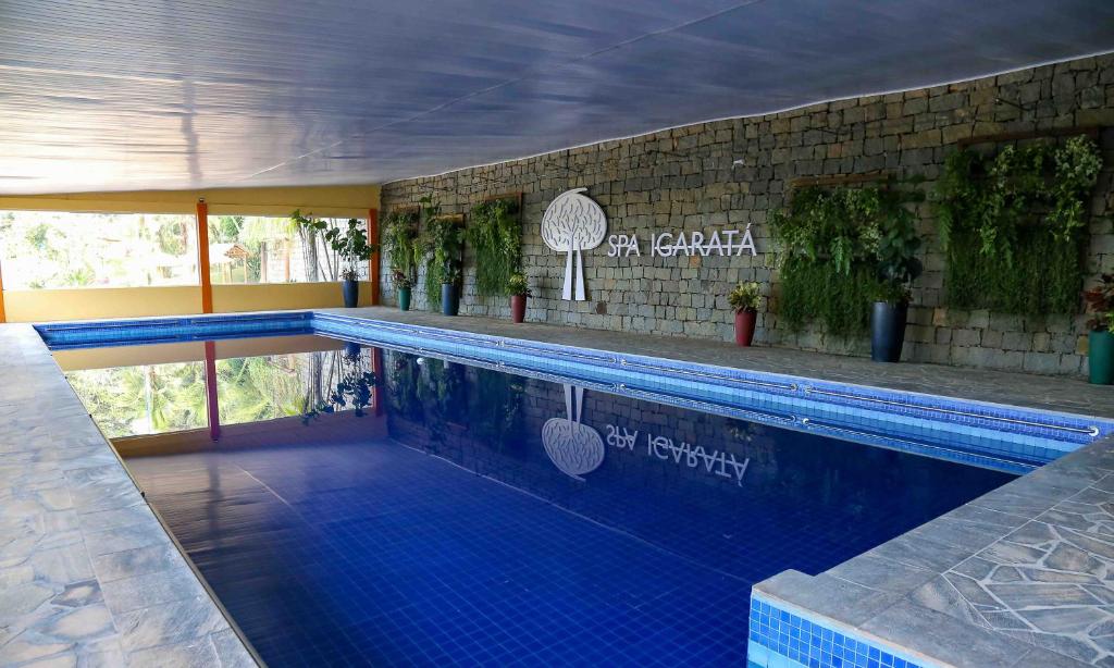 Uma piscina coberta com azulejos azuis, paredes de pedra, vasos de plantas e uma placa que diz "Spa Igaratá".