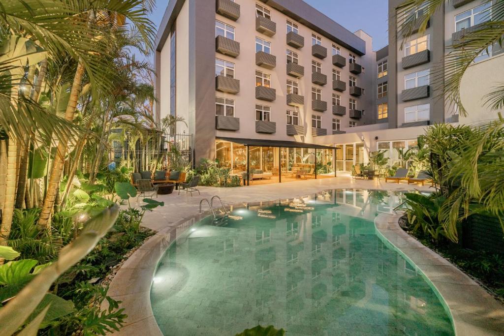 Intercity Porto Alegre Aeroporto com uma piscina externa curva cercada por plantas tropicais e grandes janelas voltadas para a área da piscina.