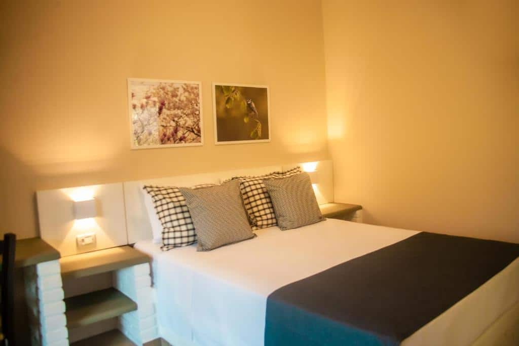 Quarto do Matiz Igaratá Resort, Spa e Eventos com uma cama bem arrumada, travesseiros xadrez, duas luminárias de parede e fotos emolduradas acima da cabeceira em um quarto bege.