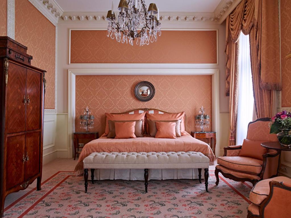 Quarto elegante no Grand Hotel Wien com paredes cor de pêssego, um lustre, uma cama de casal, poltrona e móveis de madeira ornamentados em estilo clássico, para representar onde ficar em Viena.