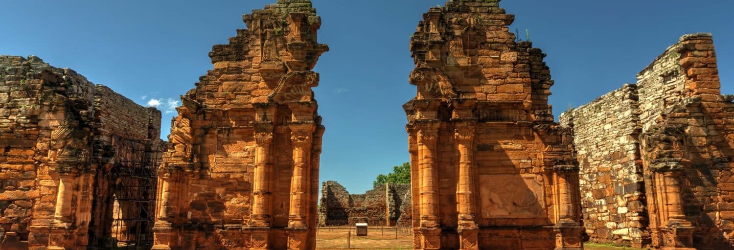 Duas ruínas de pedra altas e desgastadas, com esculturas, estão lado a lado sob um céu azul claro. - Excursão às ruínas de San Ignacio e às minas Wanda