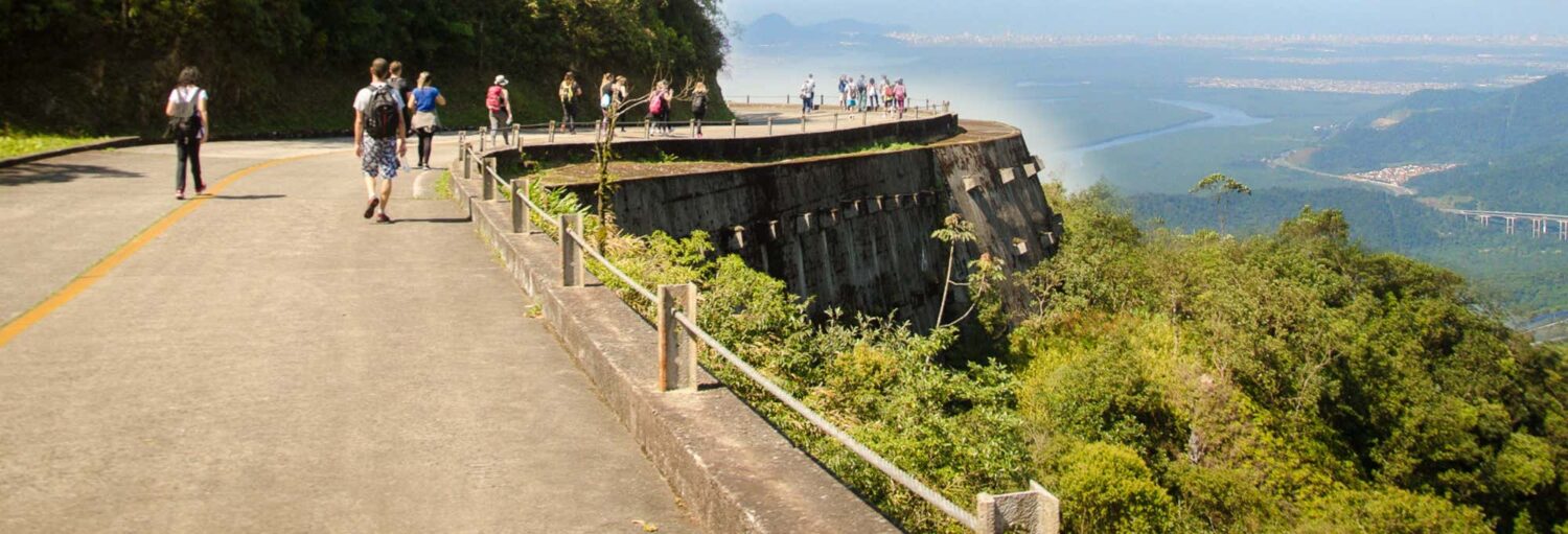 As pessoas caminham em uma trilha privada pela Estrada Velha de Santos com vistas panorâmicas das montanhas e da cidade abaixo.