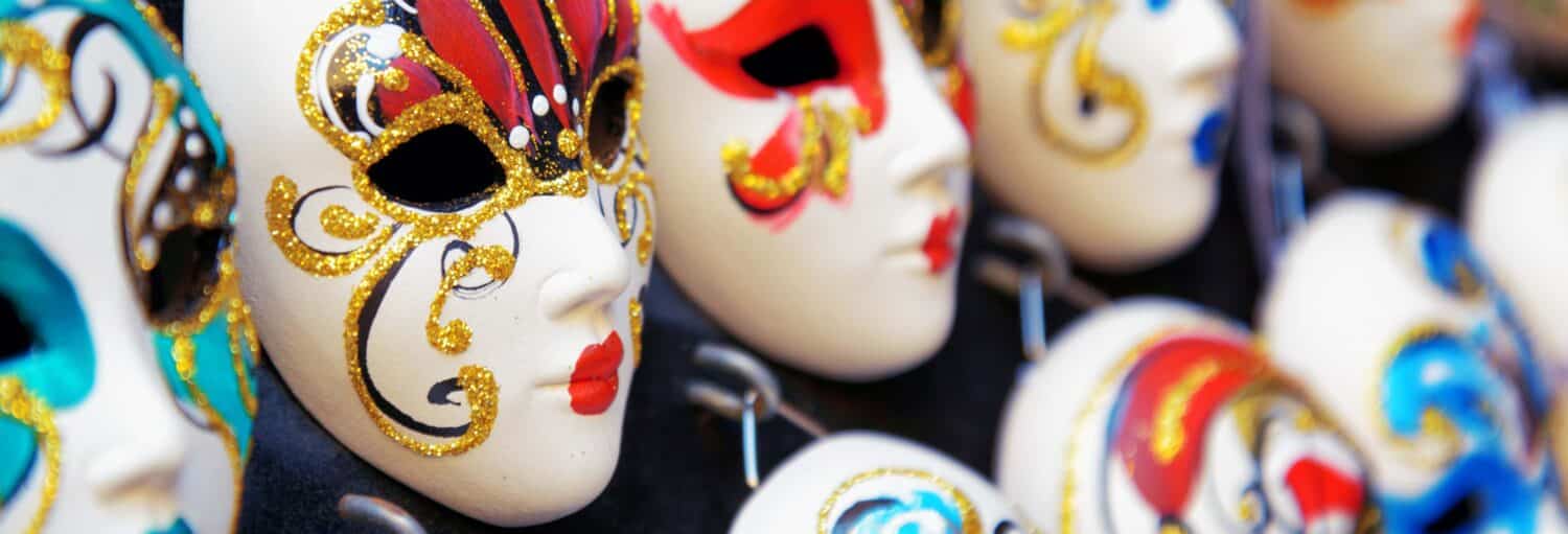 Máscaras venezianas coloridas de uma oficina de máscaras venezianas são exibidas em uma fileira com padrões e brilhos exclusivos.