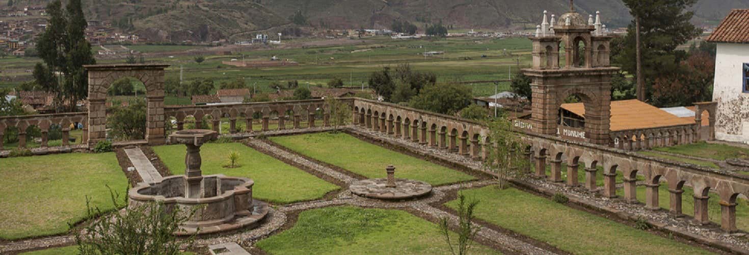 Um pátio de pedra com uma fonte central, cercado por colunas, situado em um vale verde com montanhas ao fundo na Excursão a Tinta + Fazenda de San Lorenzo de Valleumbroso