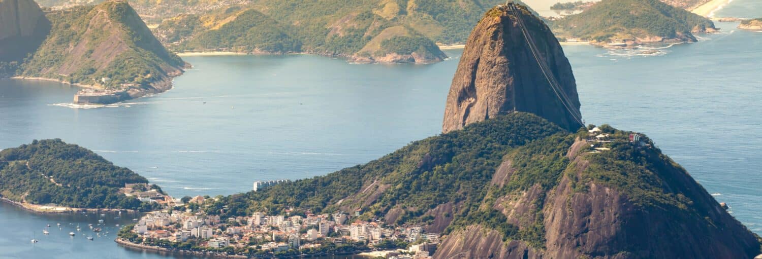 Vista aérea do Pão de Açúcar com água, vegetação e prédios da cidade no Rio de Janeiro, Brasil. A imagem ilustra o post sobre Cristo do Corcovado e Pão de Açúcar.