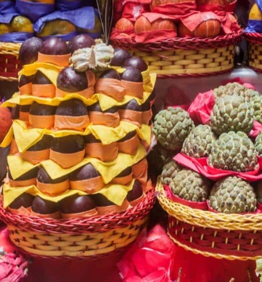 Várias frutas tropicais coloridas exibidas em cestas de tecido em um mercado, algumas embrulhadas em papel e outras em embalagens plásticas. A imagem ilustra o post sobre Tour gastronômico privado por São Paulo.