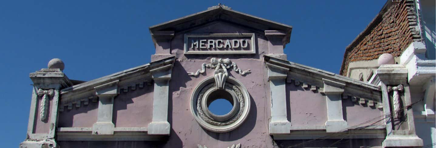 A fachada de um prédio antigo chamado "Mercado" com uma janela redonda e detalhes arquitetônicos decorativos. A foto é capa do post do Tour pelo Mercado de Pulgas.