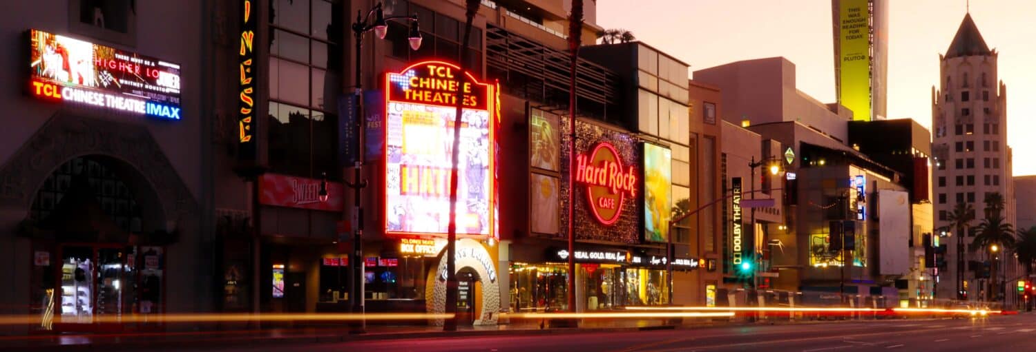 Hollywood Boulevard ao pôr do sol, mostrando o TCL Chinese Theatre e o Hard Rock Cafe com letreiros de neon e vitrines iluminadas. A foto é capa do post do Tour dos mistérios e lendas de Los Angeles.
