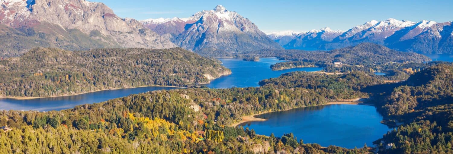 Paisagem montanhosa com vários lagos, floresta verde densa e picos cobertos de neve sob um céu azul claro do Tour panorâmico pelo Circuito Chico de Bariloche