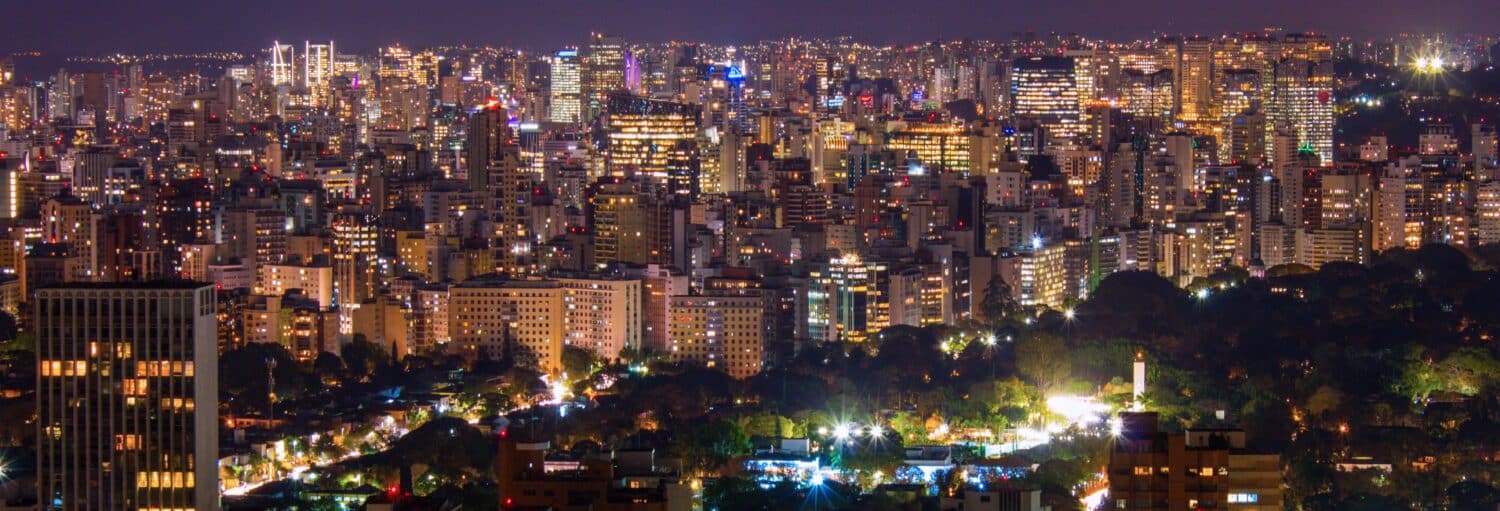 Paisagem urbana à noite com muitos prédios iluminados, arranha-céus e luzes brilhantes espalhadas pelo horizonte. A imagem ilustra o post sobre Tour privado pelos bares de São Paulo.