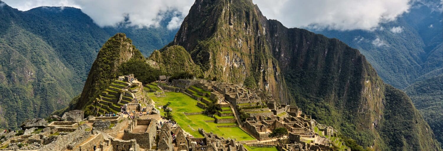 Vista das ruínas de Machu Picchu com estruturas de pedra, terraços verdes e montanhas ao fundo sob um céu nublado no Tour privado por Machu Picchu